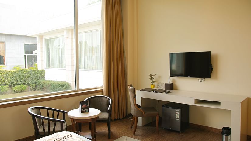 Image of a room featuring a TV below which a work desk is placed and a sitting space with two chairs and coffee table next to the window