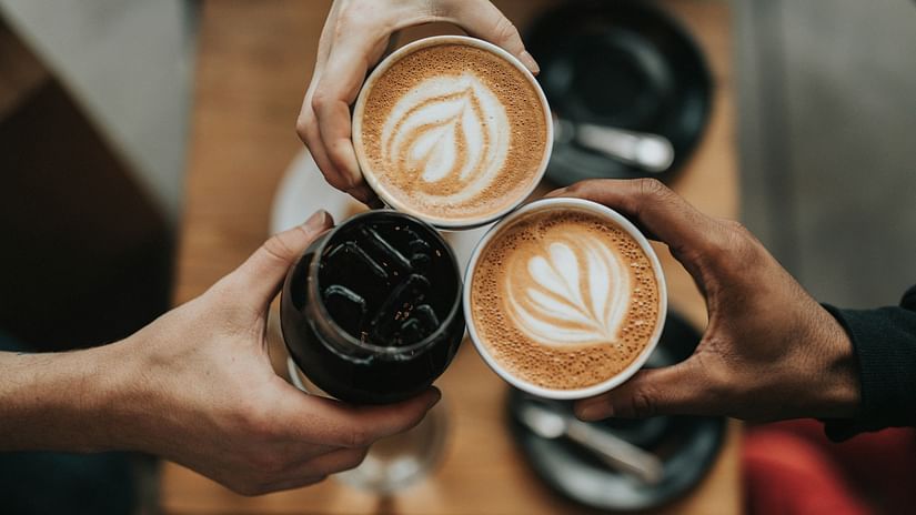 Two individuals holding cups filled with coffee, while another person holds a jar of coffee beans.