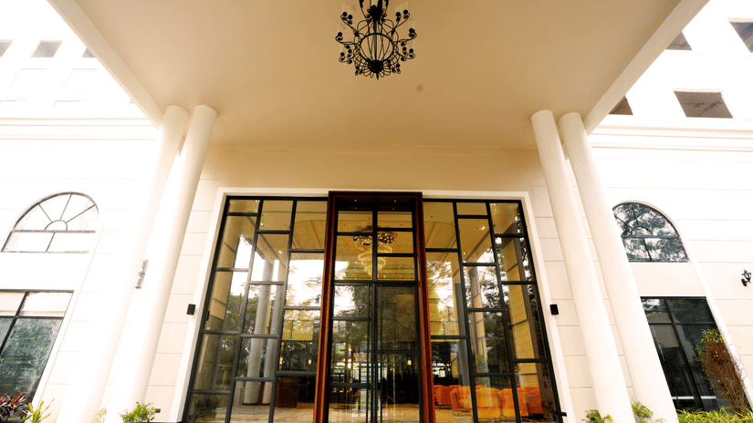Grand porte-cochere entrance at Polo Hotel, Agartala with tall white columns, glass doors and an ornate black chandelier under the canopy.