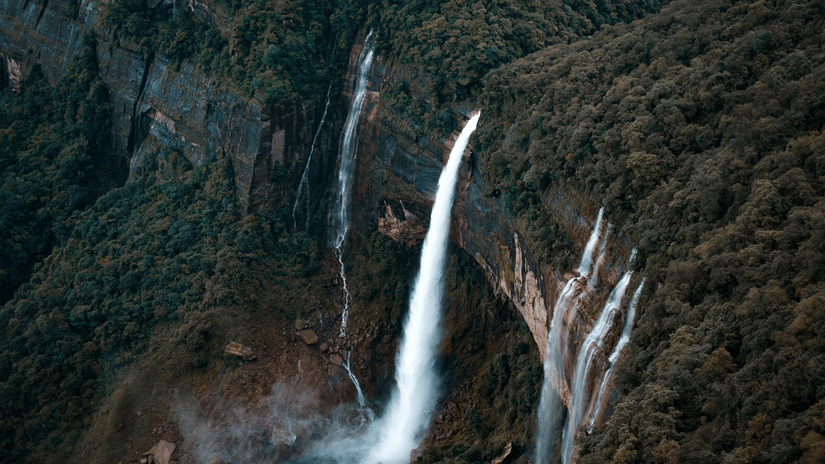 Aerial view of Nohkalikai Falls plunging from a forested clifftop into a turquoise plunge pool surrounded by deep green Khasi mountainsides.