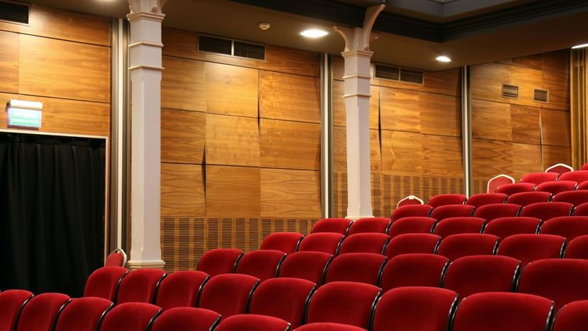 An empty theatre with rows of plush red seats and wooden panelling on the walls.