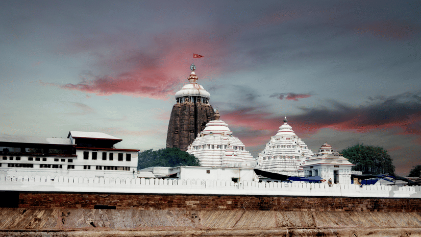 A wide view shows a temple complex with a high central tower and smaller white domes behind a long wall. The sky has streaked clouds.