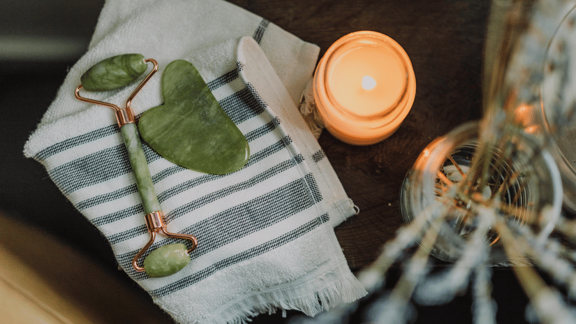 A jade roller, a gua sha, and a burning candle on a wooden table.