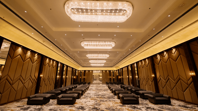 Pride Premier Alwar | a banquet hall with several chairs, decorated walls and chandeliers.