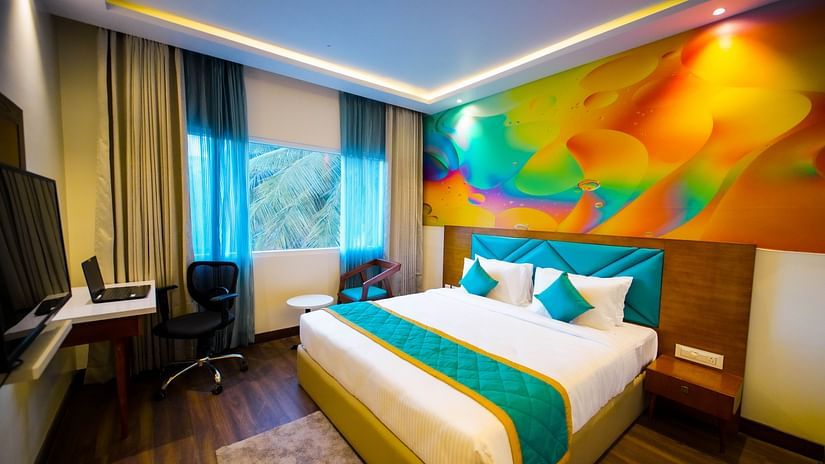 Vibrant king-size bedroom with a colorful feature wall, modern furnishings, and scenic window view at Quality Inn Rockwell Grand, Bangalore. 