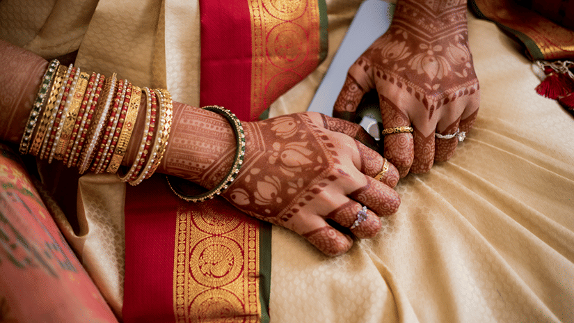A bride wearing a wedding saree while decked with bangles and mehendi on her hands