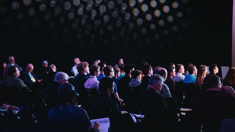 a dim-lit conference hall with people attending a symposium
