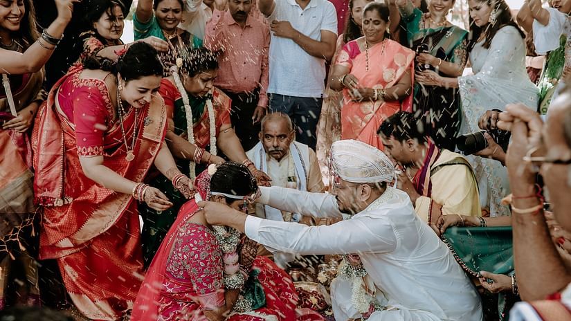 a south indian wedding inside a kalyana mandapam where the groom is putting a garland on the bridge