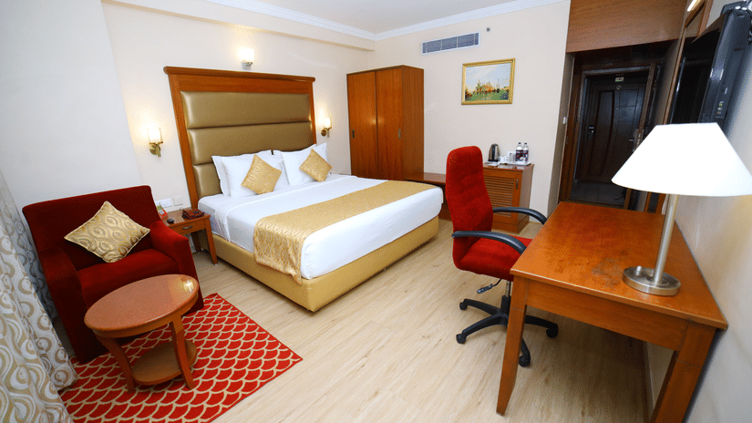 Bedroom with large bed, desk, red chair, and small seating area.