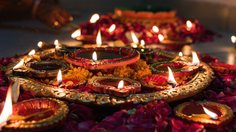 Rows of colourful oil lamps arranged on a bed of flowers during a festive celebration