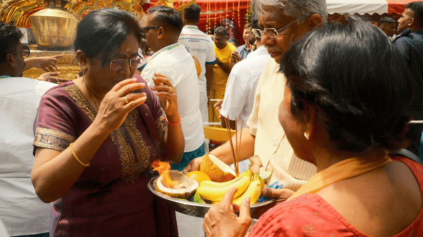 People are gathered around a food stall or offering table during a ceremony.