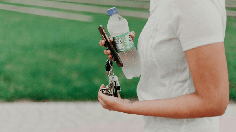 A person is holding a water bottle, a phone, and keys.