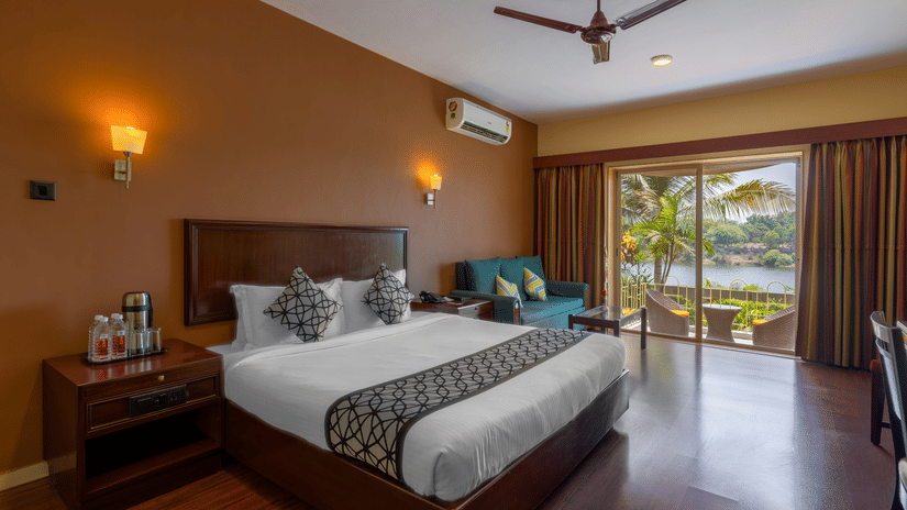 An image of a bedroom with king size bed with bedside tables, lamps, cabinets. and an open window - Ras by Treat Resorts