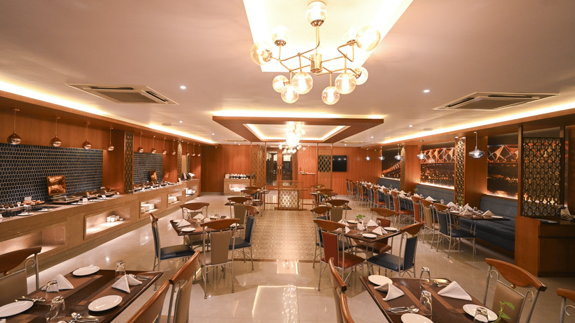 Elegant restaurant dining hall at Rivera Sarovar Portico, Ahmedabad featuring neatly arranged dining tables, decorative chandeliers and contemporary interiors.