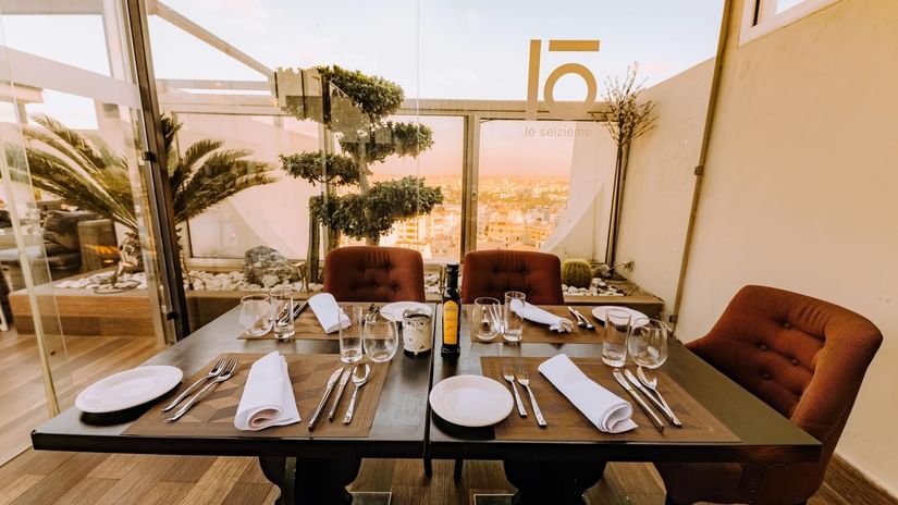 Outdoor dining setup with a view of sunset and palm trees at a rooftop restaurant.