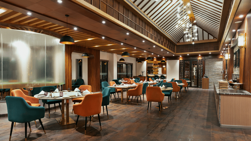 Guras Restaurant dining area at Royal Tulip Shivapuri National Park - Kathmandu with teal and orange chairs, wooden floors, and high ceilings.
