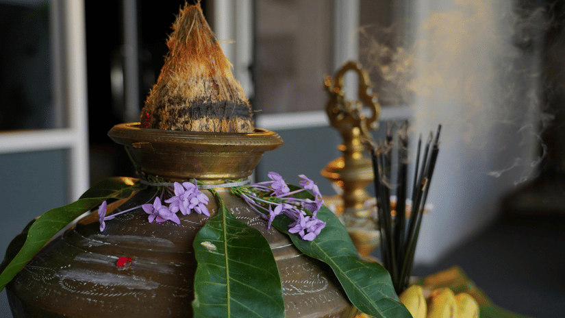 A close-up shot of a traditional ritual setup shows a brass pot and fresh flowers.