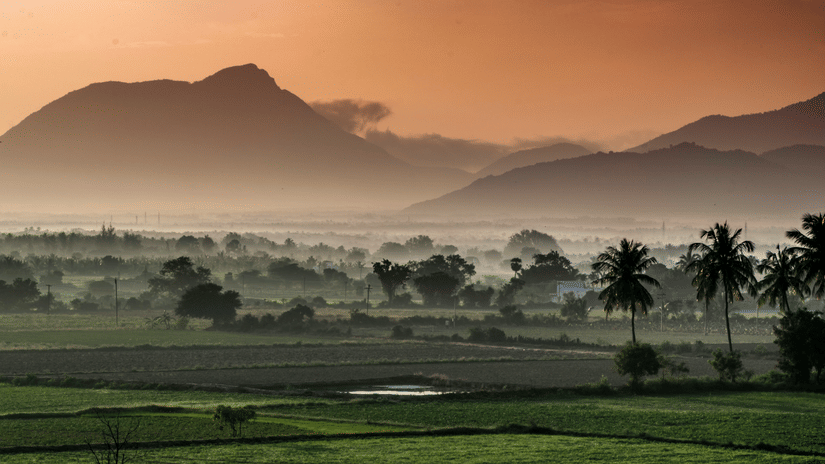 A serene landscape features mist-covered fields and mountains during a sunrise.