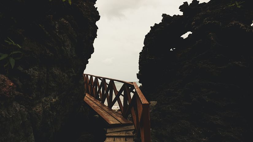 a wooden pathway next to rocky mountains with clouds in the background