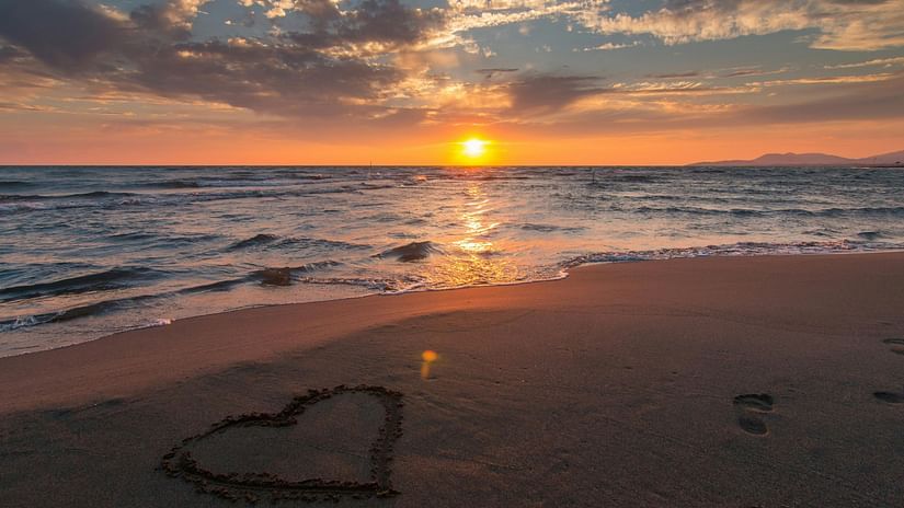 A heart drawn in the sand as the sun sets over a peaceful beach.