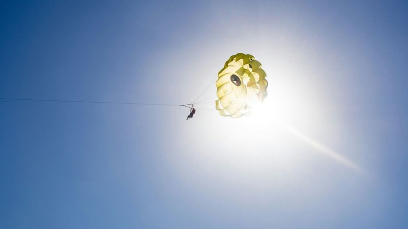 a person parasailing holding on to the harness of the parachute with the sun in the background