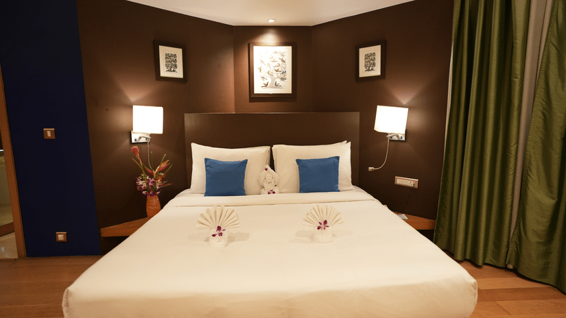Suite room at The Beatle Hotel, Powai featuring a double size bed, with bedside table with lamps on either side, and a huge curtain on one side.