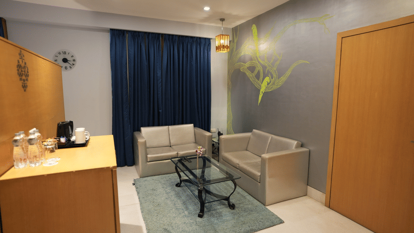 A room at The Beatle Hotel, Powai with two couches, carpet, a glass table and cupboard. 