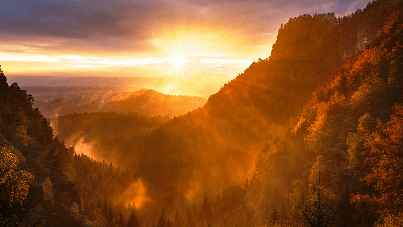 An image of sunrise over the mountains, with vibrant orange and yellow hues peeking between the peaks