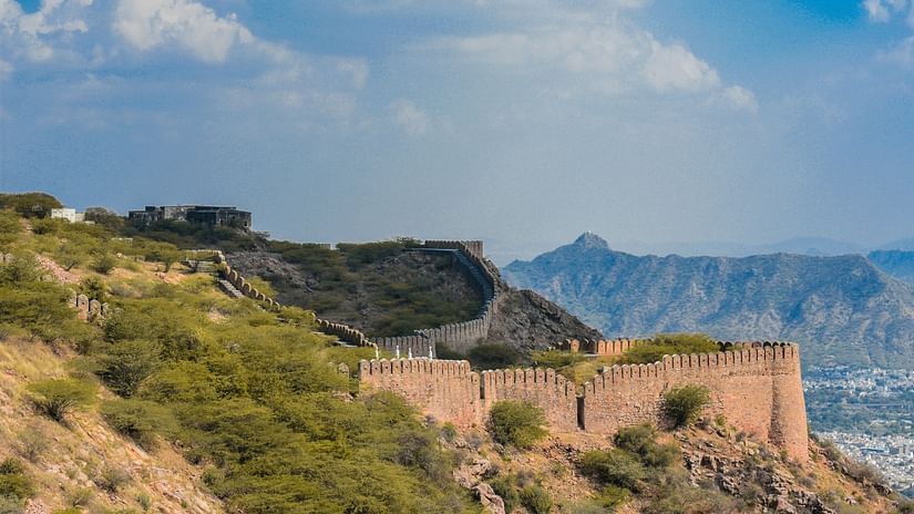 A stone fortification on a lush green hillside, surrounded by rugged terrain and a bright blue sky.