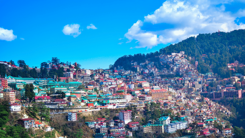 An expansive view of Shimla, showcasing densely packed colourful buildings on rolling hills