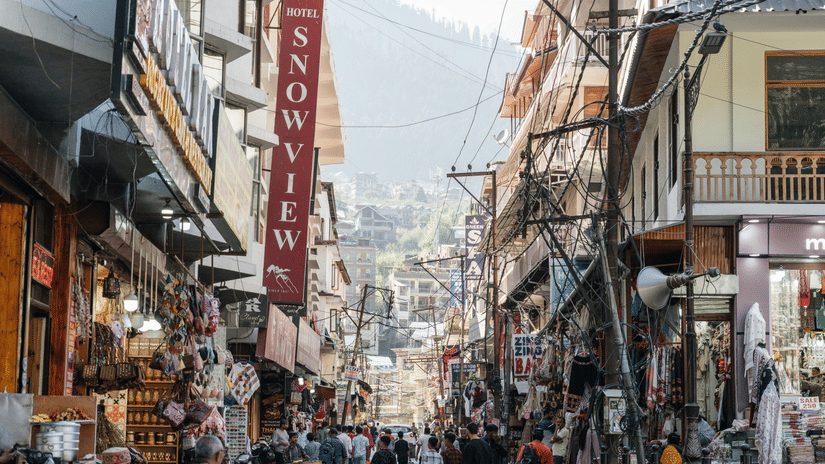 A bustling, narrow commercial street lined with tall buildings and signs, leading up a hill in a town.