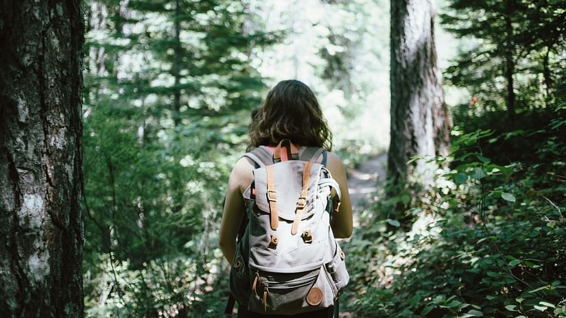 A woman walking in a path inside the forest with greenery around her