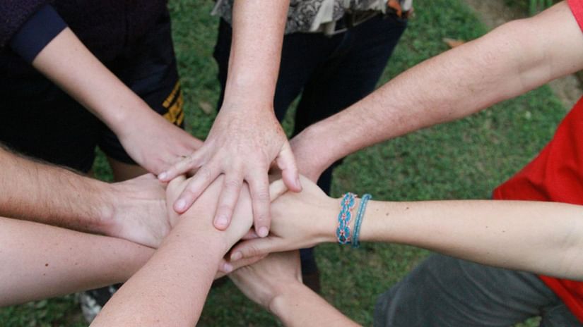A close up shot of many people joining their hands together while being in a circle.