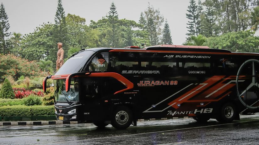 A black coloured bus parked on the road next to a garden with many trees