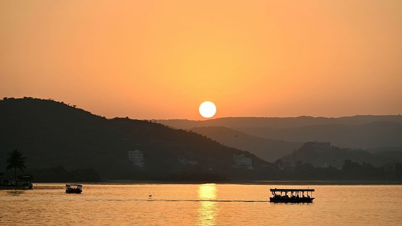 A picturesque view of lake pichola with a boat in the waters and sun setting in the background