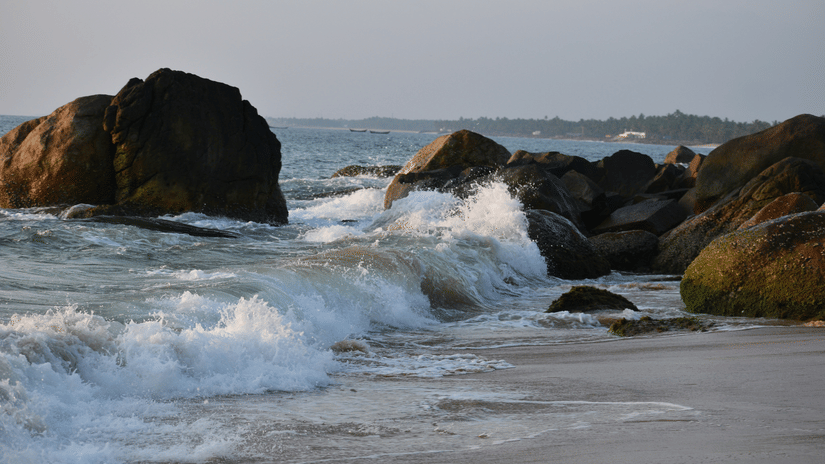Adimalathura Beach featuring waves crashing the rocky shore on a sunny day