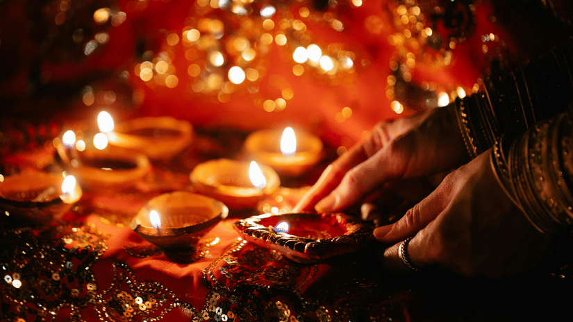 A pair of hands lighting up traditional Indian lamps as some of them are already lit