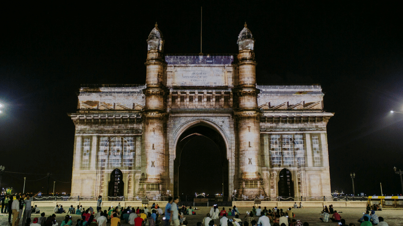 People looking at The Gateway of India at night under a clear sky
