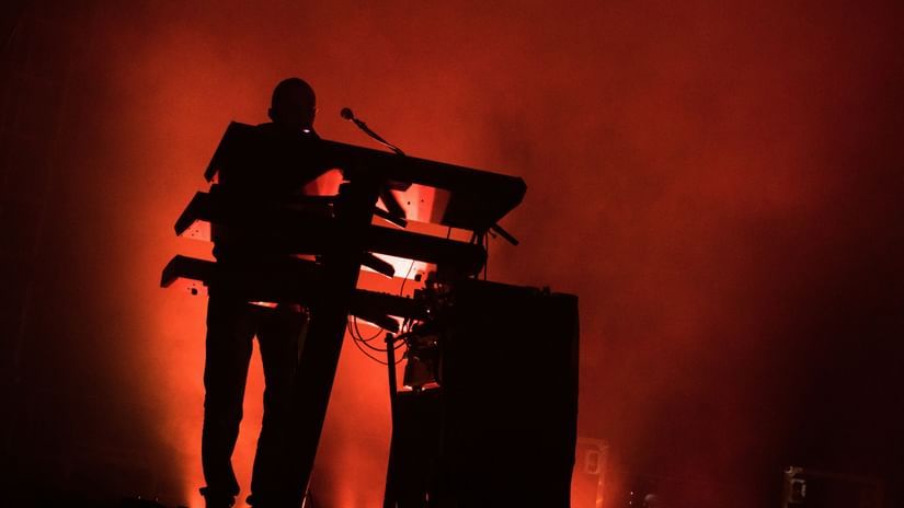 Musician performing on stage with a keyboard under red lighting.
