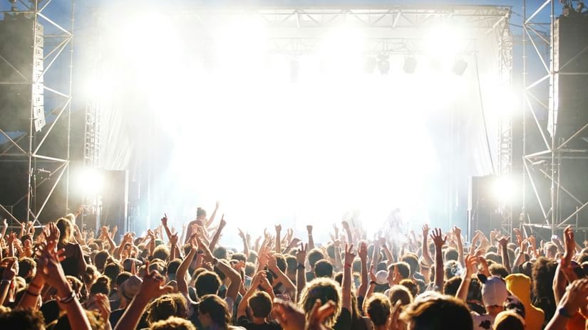 Large festival crowd cheering in front of an intensely lit stage.