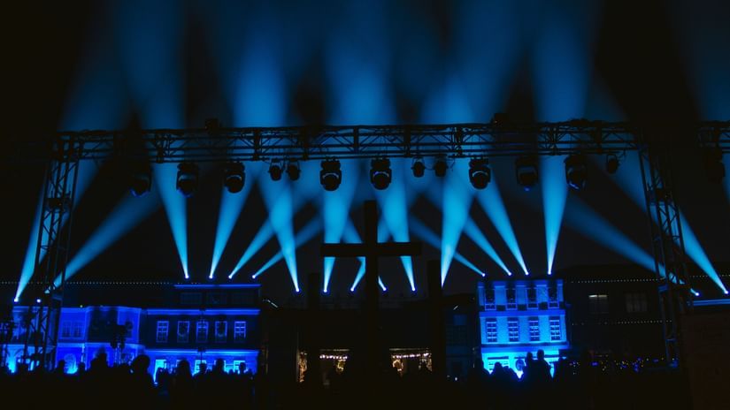 Blue-lit stage with multiple beams of light and an excited audience.
