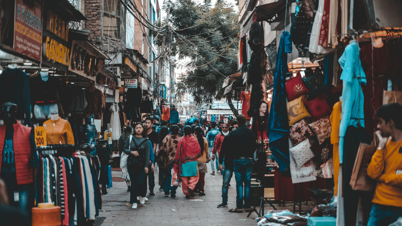 An overview of a crowded market street with people shopping and stalls on either side.