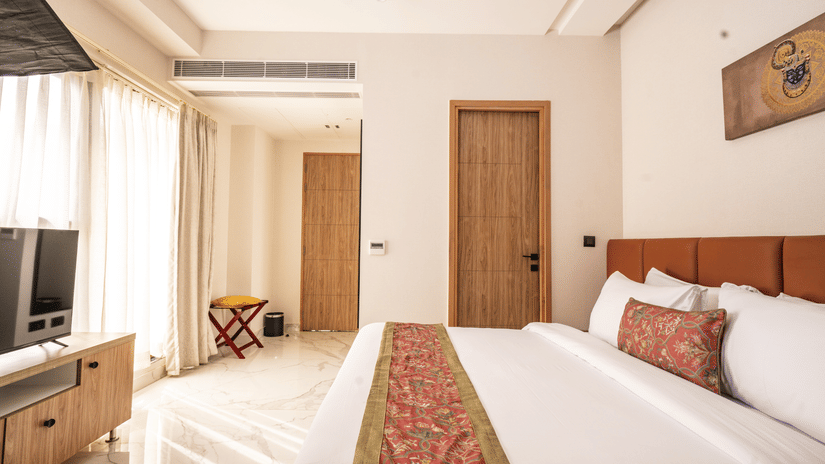 Presidential Suite at Triptam Hotel, Vrindavan featuring a plush bed facing the TV and sunlight coming through the window next to it