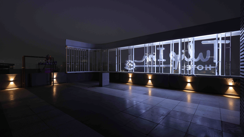 A night view of the Tulip Inn Gurugram rooftop terrace featuring a modern illuminated glass railing and warm floor lighting.