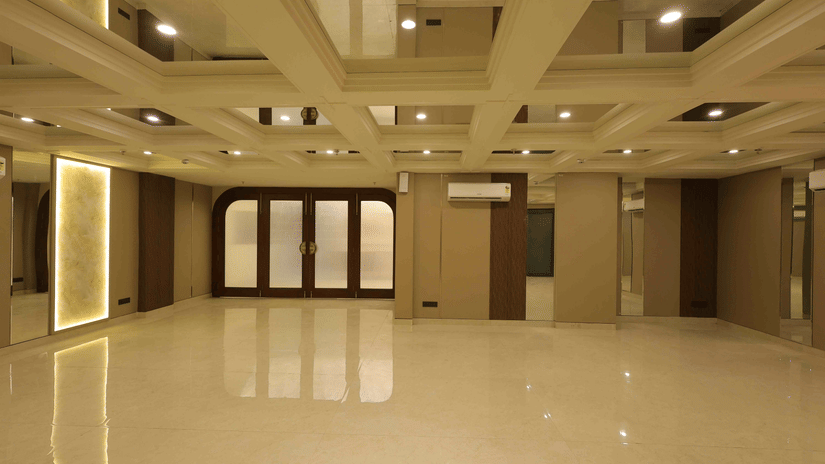 A large, empty banquet hall at Tulip Inn Gurugram with polished white floors, wood-panelled walls, and a multi-level recessed ceiling with warm lighting.