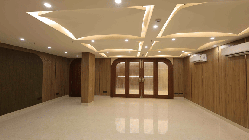 An empty banquet hall at Tulip Inn Gurugram with polished white floors, wood-paneled walls, and a decorative recessed ceiling.