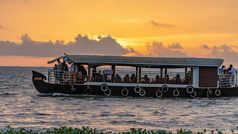 A group of people on a boat on backwater as the sun sets in a golden yellow sky