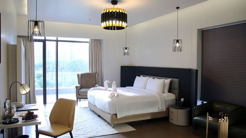 Room featuring a king-size bed next to a couch placed near the way to balcony and a work desk