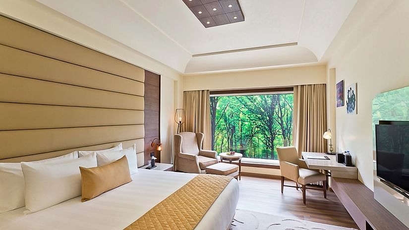 Room featuring a king-size bed in front of which a TV is mounted on the wall and sitting area next to the window with a breathtaking view of the nature