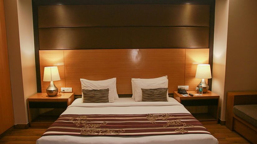 An image of a room in dim lighting featuring a plush bed with lamps on the nightstands on both sides